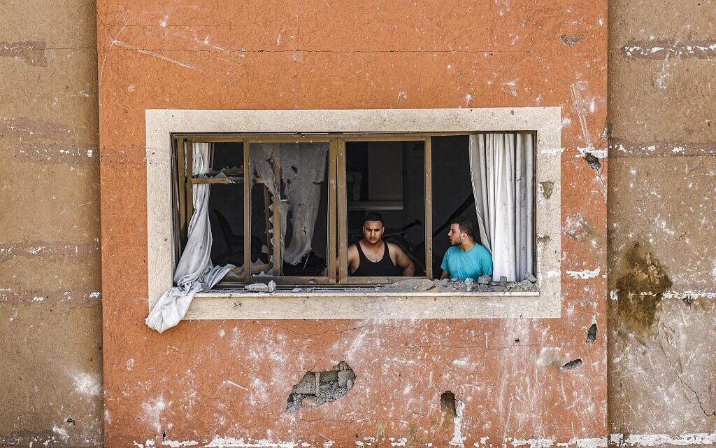 Men look out a broken window in the aftermath of an Israeli air strike in Gaza City, on August 6, 2022. The IDF has been carrying out strikes on terror targets in the enclave as rockets are fired toward Israeli communities. (Mahmud Hams/AFP)