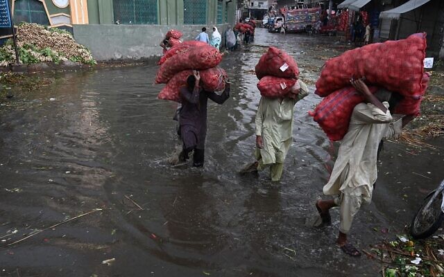 Pakistani laborers carry sacks of potatoes as they wade through a flooded market in Lahore on August 29, 2022. (Arif Ali/AFP)