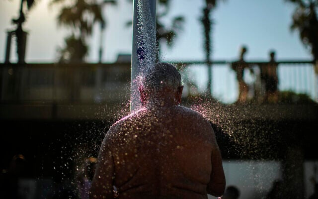 A man cools off in a public shower at a beach during a hot, sunny day in Barcelona, Spain, July 21, 2022. (AP Photo/ Francisco Seco)