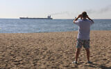A man takes a picture as the Glory bulk carrier makes its way from the port in Odesa, Ukraine, August 7, 2022. (AP/Nina Lyashonok)