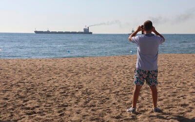 A man takes a picture as the Glory bulk carrier makes its way from the port in Odesa, Ukraine, August 7, 2022. (AP/Nina Lyashonok)