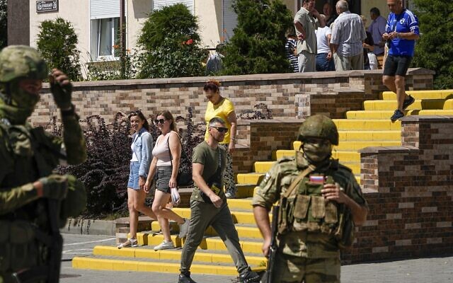 People walk past as Russian soldiers guard an office for Russian citizenship applications, in Melitopol, south Ukraine, July 14, 2022. (AP) People walk past as Russian soldiers guard an office for Russian citizenship applications, in Melitopol, south Ukraine, July 14, 2022. (AP)