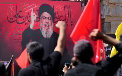 Hezbollah leader Sheik Hassan Nasrallah speaks via a video link, as his supporters raise their hands, during the Shiite holy day of Ashura, in the southern suburb of Beirut, Lebanon, August 9, 2022. (AP Photo/Hussein Malla)
