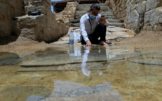 Syrian Christian Zuhair Al-Sahawi immerses his hand in water at the Bethany Beyond the Jordan baptismal site on the east bank of the Jordan River in Jordan, June 8, 2022. (AP Photo/Raad Adayleh)