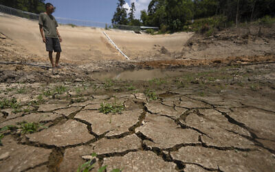 A man stands in the basin of a community reservoir near his farm that ran nearly empty after its retaining wall started to leak and hot weather and drought conditions accelerated the loss of water, in Longquan village in southwestern China's Chongqing Municipality, Aug. 20, 2022. (Mark Schiefelbein/AP)
