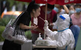 A worker wearing a protective suit swabs a woman's throat for a COVID-19 test at a coronavirus testing site in Beijing, Friday, August 26, 2022. (AP Photo/Mark Schiefelbein)