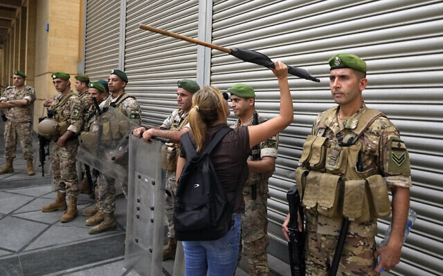 A bank customer bangs on a metal walls of a bank as army soldiers stand guard near Lebanon's parliament during a protest against a capital controls draft law protesters said would further restrict their trapped savings in the banks, in Beirut, Lebanon, Tuesday, Aug. 30, 2022. (AP Photo/Bilal Hussein)