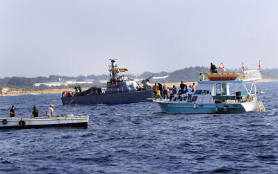 Lebanese protesters sail near an Israeli Navy vessel during a demonstration Lebanese protesters on a motorboat carry their national flag as they sail in front of an Israeli Navy vessel during a demonstration backing Lebanon's claims to disputed maritime oil and gas fields, near the southern border town of Naqoura, Lebanon, September 4, 2022. (AP/Mohammed Zaatari)
