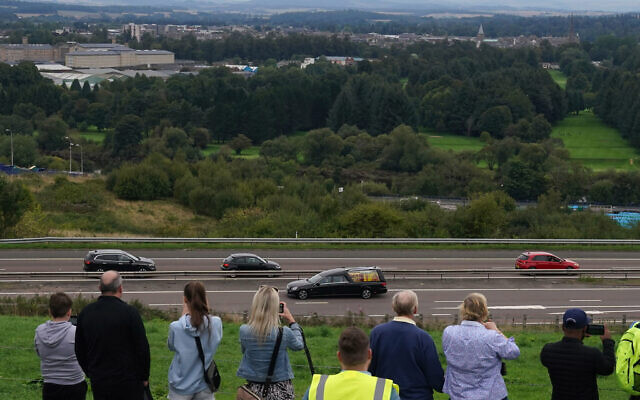 People watch the hearse carrying the coffin of Queen Elizabeth II, draped with the Royal Standard of Scotland, after it crossed Friarton Bridge as it continues its journey to Edinburgh from Balmoral, in Perth, Scotland, September 11, 2022. (Andrew Milligan/PA via AP)