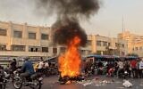A picture obtained by AFP outside Iran, shows people gathering next to a burning motorcycle in the capital Tehran on October 8, 2022. (AFP)
