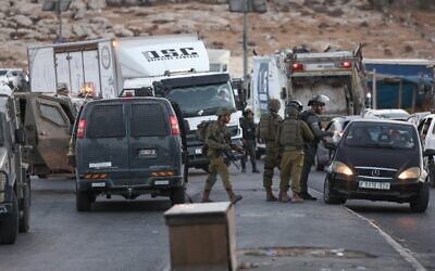 Israeli security forces talk to passengers in traffic, October 9, 2022, after closing an entrance to the Palestinian town of Anata in the West Bank, as they conducted a manhunt for the suspected shooter in a deadly attack on Saturday, October 8, 2022, in which a female soldier was killed. (Ahmad Gharabli/AFP)
