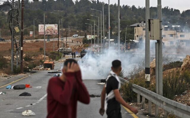 Illustrative: Young Palestinians run from tear gas fired by Israeli security forces during clashes at the northern entrance to the West Bank city of Ramallah, on October 12, 2022. (Abbas MOMANI / AFP) Illustrative: Young Palestinians run from tear gas fired by Israeli security forces during clashes at the northern entrance to the West Bank city of Ramallah, on October 12, 2022. (Abbas MOMANI / AFP)