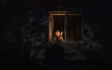 A woman looks out the window while holding a candle for light inside her house during a power outage, in Borodyanka, Kyiv region, Ukraine, October 20, 2022. (AP Photo/ Emilio Morenatti)