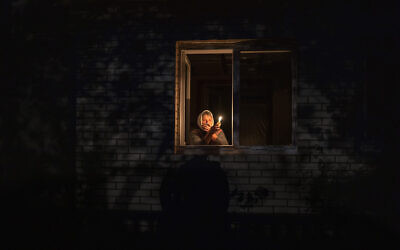 A woman looks out the window while holding a candle for light inside her house during a power outage, in Borodyanka, Kyiv region, Ukraine, October 20, 2022. (AP Photo/ Emilio Morenatti)