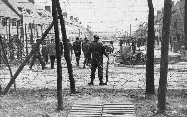 An armed sentry stands guard as civilian aliens, interned by England, walk inside an internment camp in the UK, June 2, 1940. (AP)