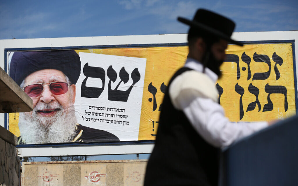 File: An ultra-Orthodox Jewish man walks near a billboard describing a picture late Shas spiritual leader Rabbi Ovadia Yosef, as part of Shas election campaign, in the northern Israeli city of Safed, February 28, 2020. (David Cohen/Flash90) File: An ultra-Orthodox Jewish man walks near a billboard describing a picture late Shas spiritual leader Rabbi Ovadia Yosef, as part of Shas election campaign, in the northern Israeli city of Safed, February 28, 2020. (David Cohen/Flash90)