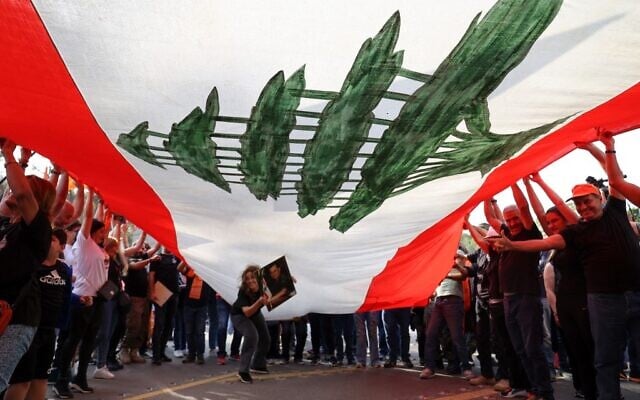 Supporters of Lebanon's President Michel Aoun cheer under a large national flag, as he prepares to leave the presidential palace in Babbda at the end of his mandate, east of the capital Beirut, on October 30, 2022. (Anwar Amro / AFP) Supporters of Lebanon's President Michel Aoun cheer under a large national flag, as he prepares to leave the presidential palace in Babbda at the end of his mandate, east of the capital Beirut, on October 30, 2022. (Anwar Amro / AFP)