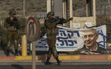 Israeli soldiers gesture to a vehicle at Tapuah Junction, next to a campaign poster for opposition leader Benjamin Netanyahu near the West Bank town of Nablus, October 16, 2022. (Tsafrir Abayov/AP)