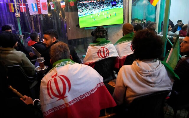 Lebanese soccer fans of Iran's team cover their backs with Iranian flags, as they sit at a coffee shop smoking water pipes and watch the World Cup group B soccer match between Iran and the United States, in the Hezbollah stronghold in the southern suburbs of Beirut, Lebanon, Tuesday, Nov. 29, 2022. (AP/Hussein Malla) Lebanese soccer fans of Iran's team cover their backs with Iranian flags, as they sit at a coffee shop smoking water pipes and watch the World Cup group B soccer match between Iran and the United States, in the Hezbollah stronghold in the southern suburbs of Beirut, Lebanon, Tuesday, Nov. 29, 2022. (AP/Hussein Malla)