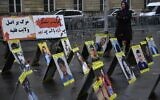 A protester stands next to placards with portraits of the victims of Iran's repression, near the French National Assembly in Paris on December 6, 2022. (Julien De Rosa/AFP)