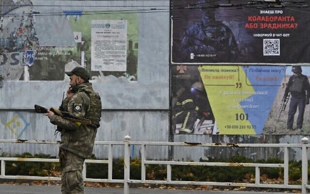 A Ukrainian policeman speaks on his phone next to a poster (R, up) calling on residents to denounce those who collaborated with the Russian forces during their occupation of the city, Kherson, December 8, 2022, (Genya SAVILOV/AFP) A Ukrainian policeman speaks on his phone next to a poster (R, up) calling on residents to denounce those who collaborated with the Russian forces during their occupation of the city, Kherson, December 8, 2022, (Genya SAVILOV/AFP)