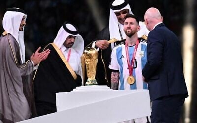 Qatar's Emir Sheikh Tamim bin Hamad al-Thani (back) wraps an abaya around Argentina's forward #10 Lionel Messi on stage next to the FIFA World Cup Trophy after Argentina won the Qatar 2022 World Cup final football match between Argentina and France at Lusail Stadium in Lusail, north of Doha on December 18, 2022. (Photo by Kirill KUDRYAVTSEV / AFP)