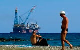 Illustrative: People on a beach as a drilling platform is seen in the background outside from Larnaca port, in the eastern Mediterranean island of Cyprus, October 15, 2017. (Petros Karadjias/AP)
