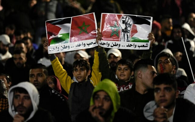 Palestinians wave banners with Moroccan and Palestinian flags as they watch a live broadcast of the World Cup quarterfinal soccer match between Morocco and Portugal played in Qatar, in the West Bank town of Nablus,  Dec. 10, 2022. Arabic on banner reads 'One people, one country'. (AP Photo/Majdi Mohammed)