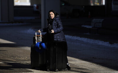 A lone traveler pushes her baggage through a shaft of daylight on her way to the shuttle bus aisle for rental cars outside Denver International Airport, December 23, 2022. (AP Photo/David Zalubowski)
