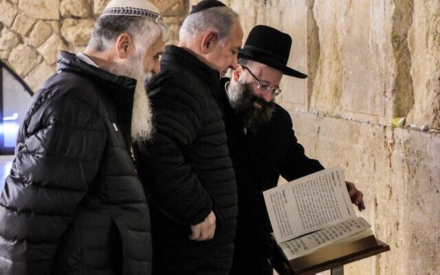 Prime Minister Benjamin Netanyahu (C) reads from the Torah at the Western Wall in Jerusalem accompanied by the Western Wall's Rabbi Shmuel Rabinovitch (R) and the CEO of the Western Wall Heritage Foundation Mordechai Eliav (L), on January 1, 2023. (GIL COHEN-MAGEN / various sources / AFP) Prime Minister Benjamin Netanyahu (C) reads from the Torah at the Western Wall in Jerusalem accompanied by the Western Wall's Rabbi Shmuel Rabinovitch (R) and the CEO of the Western Wall Heritage Foundation Mordechai Eliav (L), on January 1, 2023. (GIL COHEN-MAGEN / various sources / AFP)