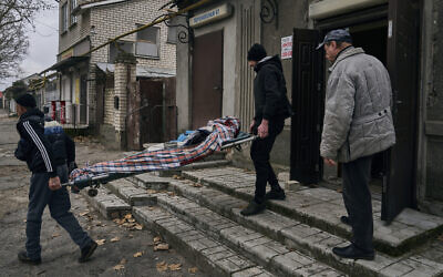 Local residents carry the body of a 20-year-old man killed in Russian shelling in Kherson, Ukraine, Thursday, January 5, 2023. (AP Photo/LIBKOS)