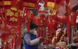 A vendor wearing a face mask checks her smartphone at her store selling Chinese Lunar New Year decorations in Beijing, January 7, 2023. (AP/Andy Wong)