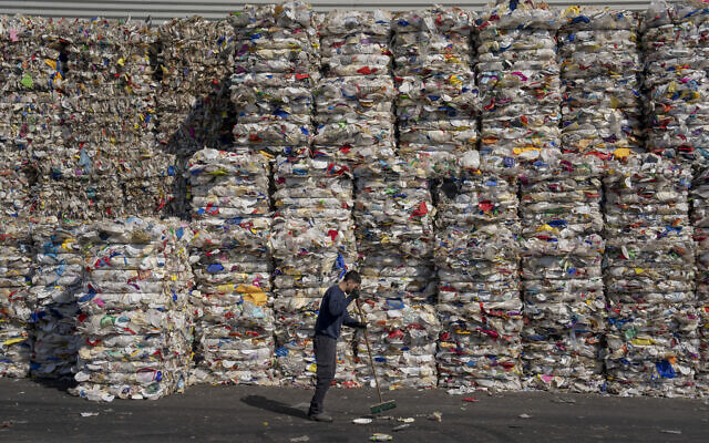 A GreenNet recycling plant employee cleans the ground next to piles of disposable plastic ready for export, in Atarot industrial zone, north of Jerusalem, January 25, 2023. (Oded Balilty/AP)