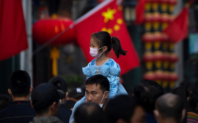 A girl wearing a face mask rides on a man's shoulders as they walk along a tourist shopping street in Beijing, October 7, 2022. (AP Photo/Mark Schiefelbein, File) A girl wearing a face mask rides on a man's shoulders as they walk along a tourist shopping street in Beijing, October 7, 2022. (AP Photo/Mark Schiefelbein, File)