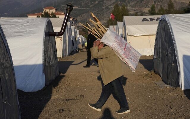A Turkish man who lost his house in the devastating earthquake, carries wood at a makeshift camp, in Iskenderun city, southern Turkey, Tuesday, Feb. 14, 2023. Thousands left homeless by a massive earthquake that struck Turkey and Syria a week ago packed into crowded tents or lined up in the streets for hot meals as the desperate search for survivors entered what was likely its last hours. (AP Photo/Hussein Malla)