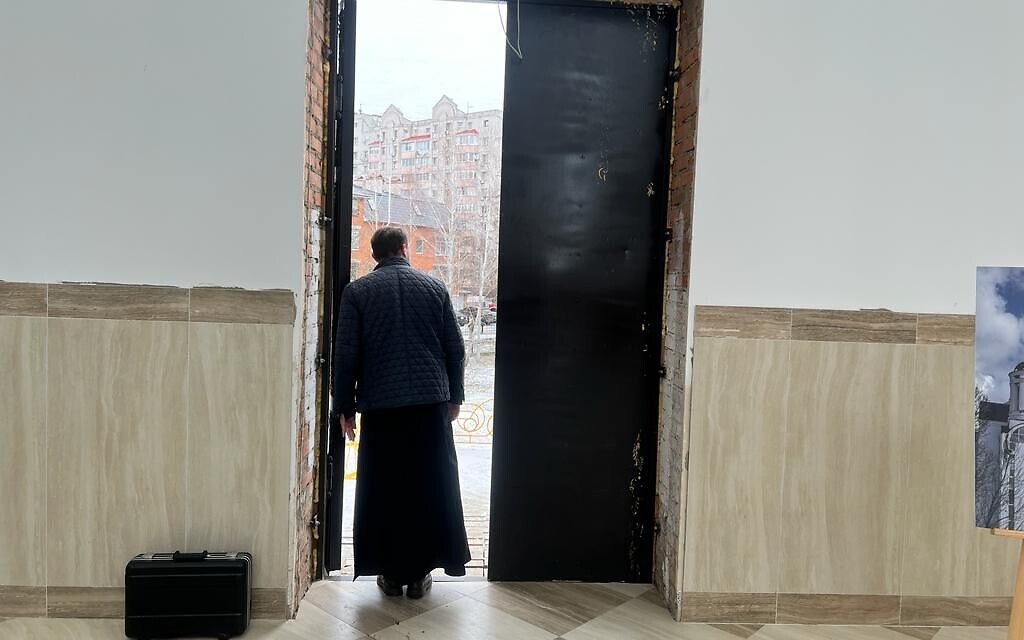 A priest watches Foreign Minister Eli Cohen's visit to Bucha, Ukraine, February 16, 2023 (Lazar Berman/The Times of Israel)