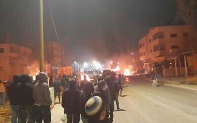 Settlers look on as cars and homes burn in the West Bank town of Huwara on February 26, 2023. (Courtesy)