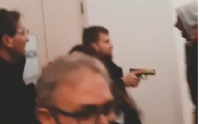 In a screenshot from video on social media, an armed guard holds a gun across from pro-BDS activists who interrupted a lecture by Israel's ambassador to Spain, Rodica Radian-Gordon, at Complutense University of Madrid, February 8, 2023. (Twitter screenshot; used in accordance with Clause 27a of the Copyright Law) In a screenshot from video on social media, an armed guard holds a gun across from pro-BDS activists who interrupted a lecture by Israel's ambassador to Spain, Rodica Radian-Gordon, at Complutense University of Madrid, February 8, 2023. (Twitter screenshot; used in accordance with Clause 27a of the Copyright Law)