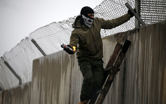 Illustrative: A Palestinian standing on a ladder tries to toss a Molotov cocktail over Israel's security barrier in the West Bank village of Bilin near Ramallah on February 7, 2020. (ABBAS MOMANI / AFP) Illustrative: A Palestinian standing on a ladder tries to toss a Molotov cocktail over Israel's security barrier in the West Bank village of Bilin near Ramallah on February 7, 2020. (ABBAS MOMANI / AFP)