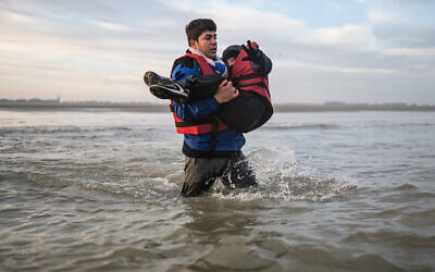 A migrant carries a child as he runs to board a smuggler's boat on the beach of Gravelines, near Dunkirk, northern France on October 12, 2022, in an attempt to cross the English Channel. (Sameer Al-Doumy/AFP)