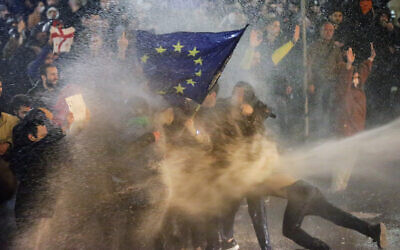 Protesters carrying a European Union flag are sprayed by a water cannon during clashes with riot police near the Georgian parliament in Tbilisi on March 7, 2023. (AFP)
