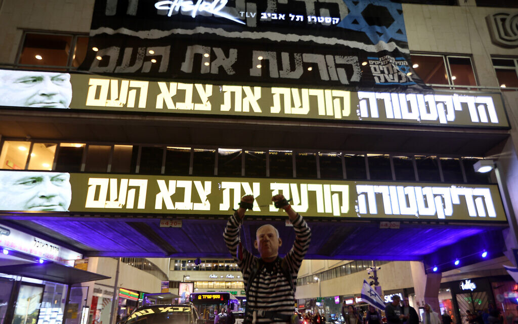 Protesters gather during a rally against the government's controversial judicial overhaul bill, in Tel Aviv on March 18, 2023. The neon slogan reads: 'The dictatorship is tearing apart the people's army.' (Jack Guez/AFP)