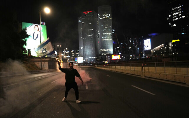 A man waves an Israeli flag as he joins other anti-government protesters in blocking the Ayalon Highway in Tel Aviv, March 11, 2023. (AP Photo/Ohad Zwigenberg) A man waves an Israeli flag as he joins other anti-government protesters in blocking the Ayalon Highway in Tel Aviv, March 11, 2023. (AP Photo/Ohad Zwigenberg)