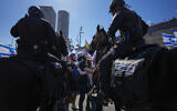 Israelis hug as they protest against plans by Prime Minister Benjamin Netanyahu's government to overhaul the judicial system while mounted policemen block their way on the main freeway in Tel Aviv, March 16, 2023. (AP Photo/Ohad Zwigenberg)