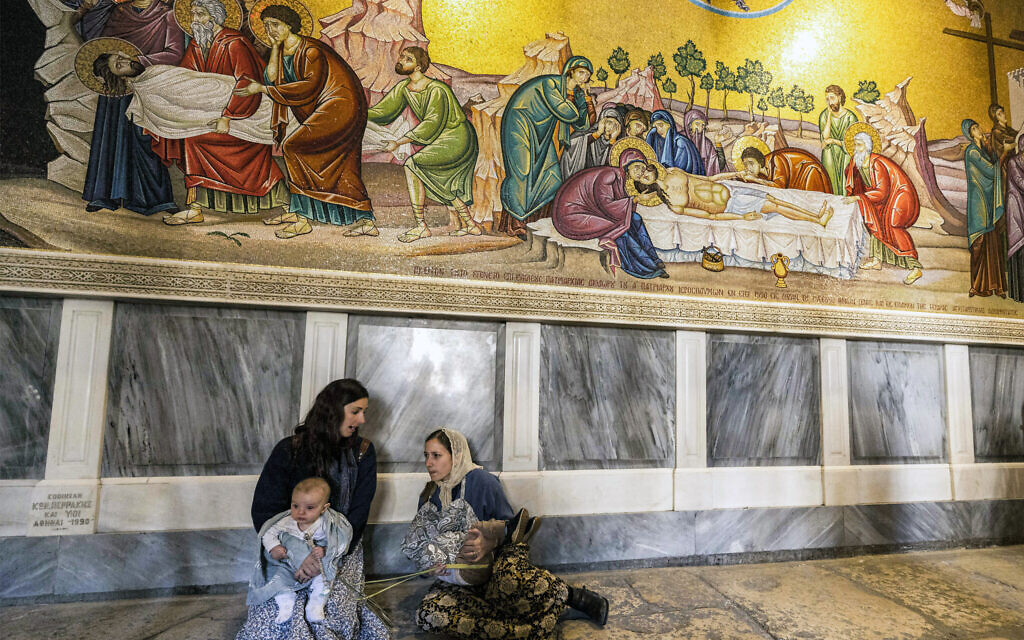 Christian pilgrims sit by a mosaic depicting the withdrawal of the body of Jesus Christ from the cross by the Unction Stone (not pictured) at the Church of the Holy Sepulchre in Jerusalem on April 2, 2023, Palm Sunday according to Catholics. (Photo by MENAHEM KAHANA / AFP)