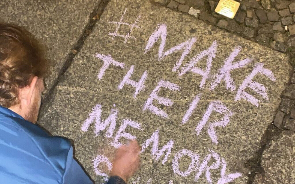 German volunteer writes a message in chalk next to cleaned Stolpersteine (stumbling stones), November 11, 2022. (Courtesy of MakeTheirMemoryShine)