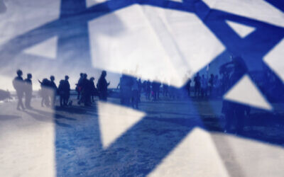 Israeli demonstrators are seen through Israel's national flag during a protest against plans by Prime Minister Benjamin Netanyahu's government to overhaul the judicial system, in Cesarea, Israel, Friday, March 17, 2023. (AP Photo/Oded Balilty)
