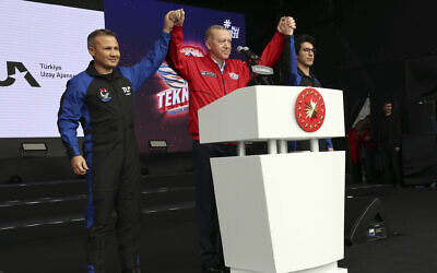 Turkey's President Recep Tayyip Erdogan (center) holds up the hands of Turkish air force pilot Alper Gezeravci (left) and aviation systems engineer Tuva Cihangir Atasever at Teknofest military fair, in Istanbul, Turkey, April 29, 2023. (Turkish Presidency via AP)