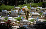 An Israeli soldier places flowers and candles on graves of fallen soldiers at the Mount Herzl Military Cemetery in Jerusalem, May 3, 2022, ahead of Memorial Day. (Yonatan Sindel/Flash90)