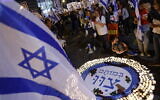 Demonstrators light memorial candles during a rally to protest the government's judicial overhaul plans, in Tel Aviv, on April 22, 2023, three days before Israel's annual memorial day for fallen soldiers. The text reads: "In their deaths, they commanded us: One Israel. Jewish. Free. Democratic" (Photo by JACK GUEZ / AFP)
